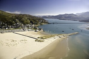 En kystby med strand, mole og bjerge i baggrunden.