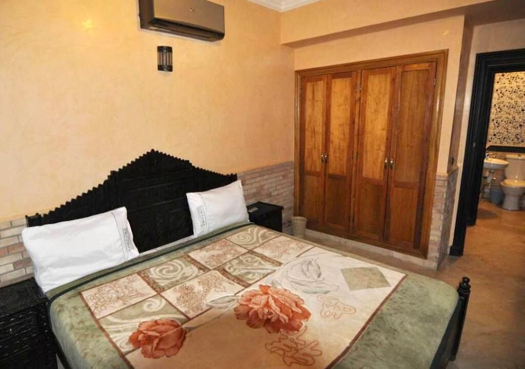 Quarto de hotel com uma cama, um guarda-roupa de madeira e um banheiro visível ao fundo.