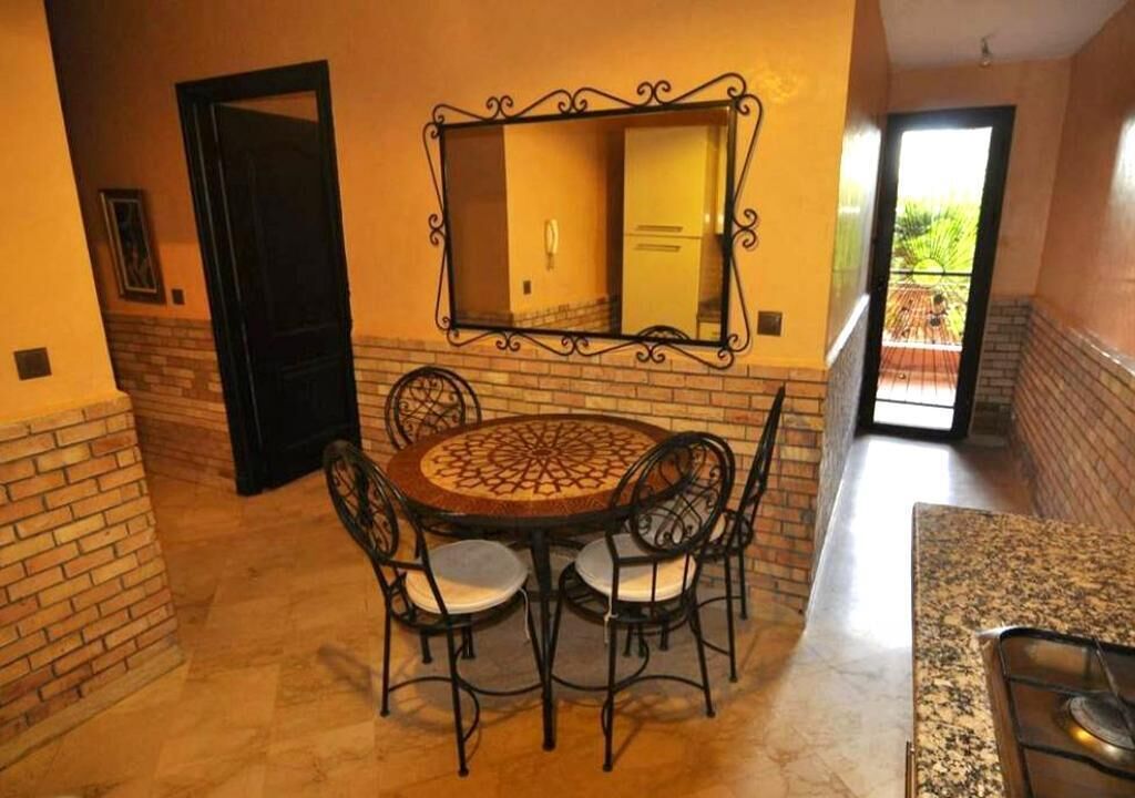 Comedor con una mesa redonda y sillas, un espejo grande sobre la mesa, y vistas al exterior a través de una puerta.