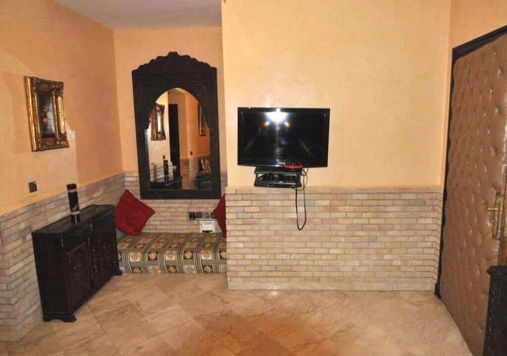 Un soggiorno con televisore montato su una parete in mattoni, un mobiletto in legno scuro e un cuscino rosso sul pavimento.