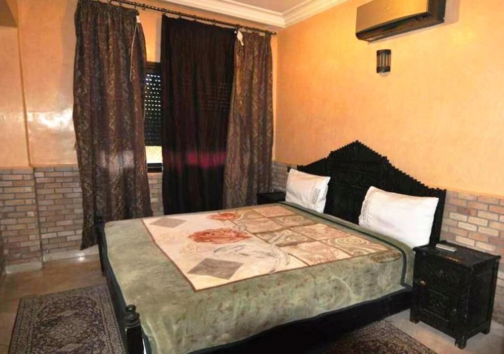 Een slaapkamer met een bed, gordijnen, een nachtkastje en een wandairconditioner.