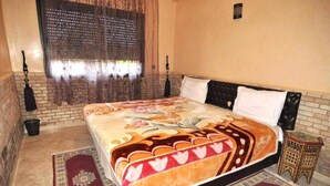 A bedroom with a large bed, a patterned bedspread, a window with curtains, a small side table, and a decorative rug. - Residence Barrone Marrakech 3384 (Marrakech)