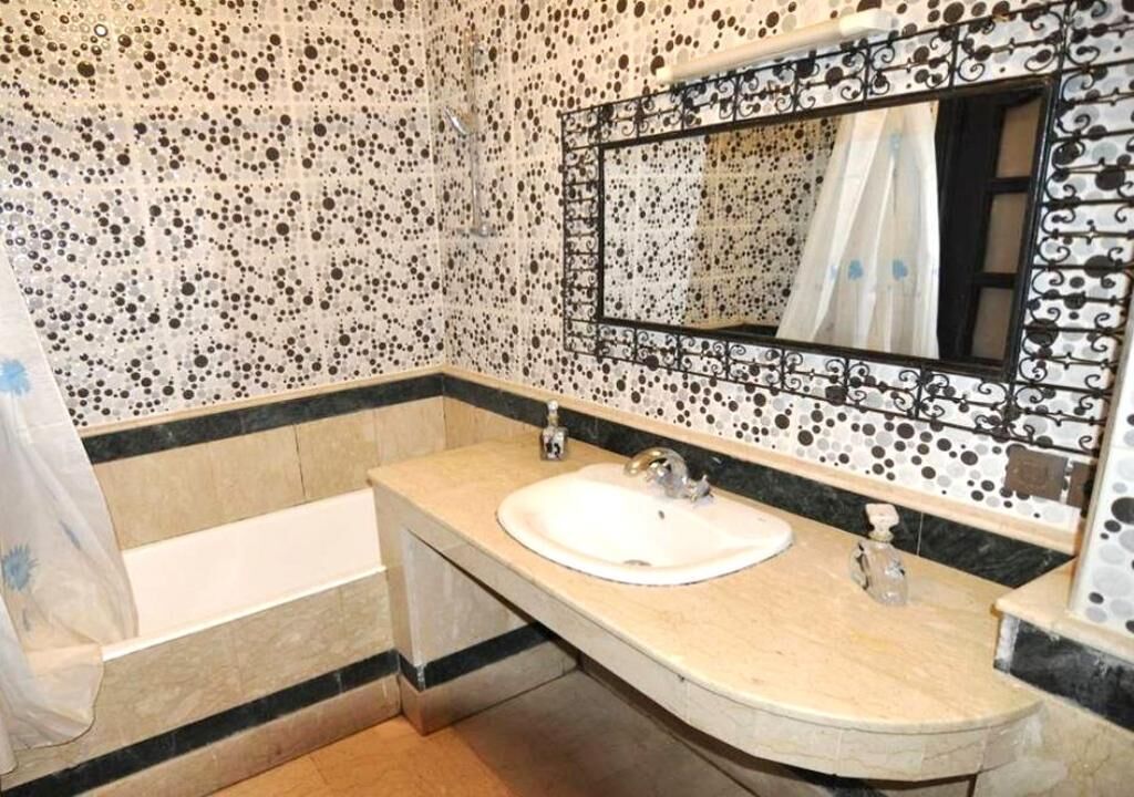 A bathroom with a white sink, a bathtub, and a mirror with a decorative frame.