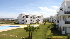 A modern hotel with multiple white buildings, a swimming pool, and a well-maintained lawn. - The Greens Residence 3633 (SAIDIA)