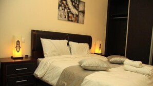 A neatly made bed with white and grey bedding, a dark headboard, and two bedside lamps. - The Greens Residence 3633 (SAIDIA)
