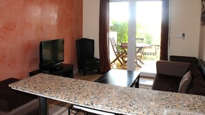 Una sala de estar con televisor, sofá, mesa y vista al exterior.