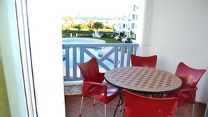 A balcony with a round table and four red chairs, overlooking a pool and buildings. - Residence Java Rasmile Mdiq 3396 (Mdiq)