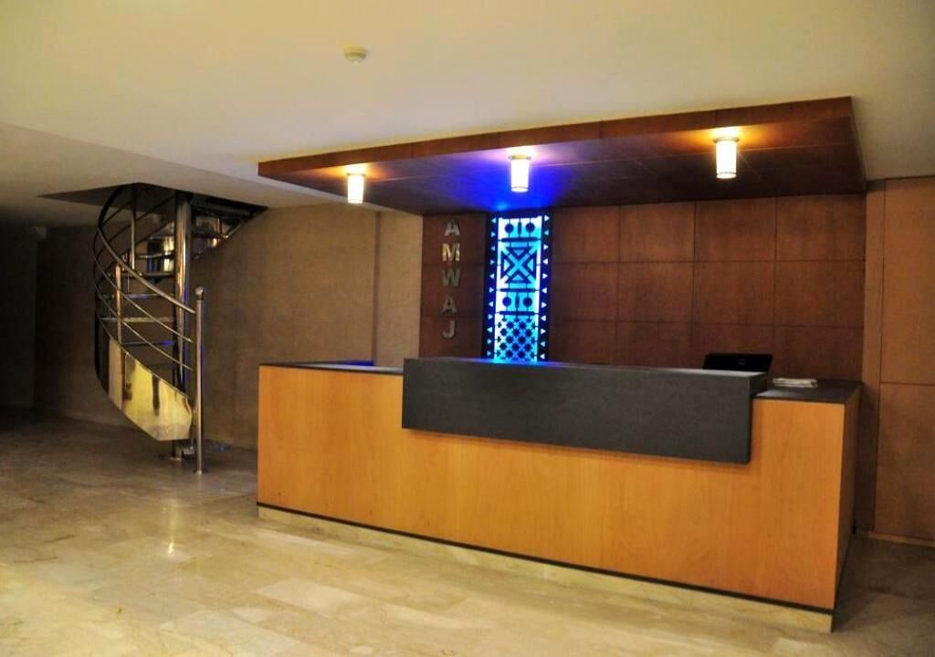 Mostrador de recepción con detalles de madera, un elemento decorativo en la pared con iluminación azul y una escalera de caracol al fondo.