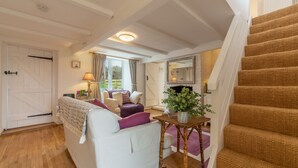 A cozy living room with a white sofa, purple cushions, a wooden table with a plant, and a staircase with brown carpet. - First & Last, Trimingham, Norfolk (Trimingham)