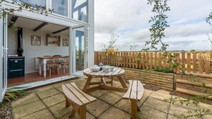 A patio with wooden benches and a table, a wooden fence, and a stone wall in the background. - First & Last, Trimingham, Norfolk (Trimingham)