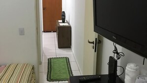 A small room with a bed, a TV, a desk, and a door leading to another room. - Espaço da Caraputinga (São Paulo)