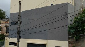A two-story building with a flat roof, a beige upper floor, and a grey lower floor. There are two garage doors on the ground floor. - Espaço da Caraputinga (São Paulo)