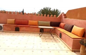 A sunlit outdoor seating area with a low wall, a table, and a potted plant. - Villa Amerchich 2968 (Marrakech)