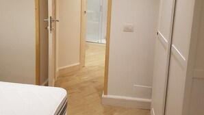 A narrow hallway with a wooden door frame, a white wardrobe, and a bed with a white mattress. - The Chiaia steps :camera white (Napoli)