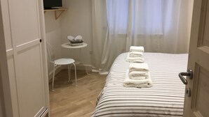 A hotel room with a bed, a small table with a basket, a chair, and a TV mounted on the wall. - The Chiaia steps :camera white (Napoli)