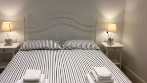 A neatly made bed with striped bedding, two bedside tables with lamps, and a heart-shaped lamp base on each table. - The Chiaia steps :camera white (Napoli)