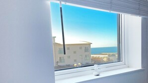 Ein Schlafzimmer mit Bett, Fenster und Blick auf Gebäude sowie ein Gewässer.