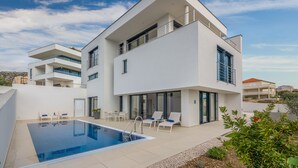 Une maison moderne à deux étages dotée d’une piscine, d’un espace salon extérieur et d’un balcon.