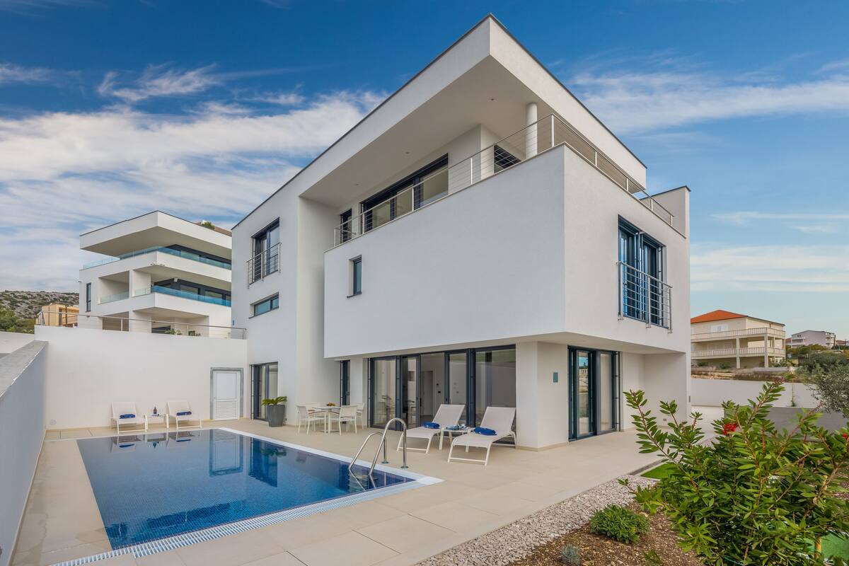 A modern two-story house with a swimming pool, outdoor seating, and a balcony.