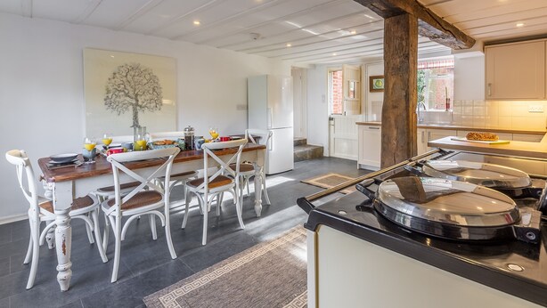 A modern kitchen with white cabinetry, a dining area with white chairs, and a large wooden beam ceiling. - The Tack House, Holkham, Norfolk (Wells-Next-The-Sea)