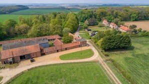 A large, open barn with a dirt driveway and a green field in the foreground. - The Tack House, Holkham, Norfolk (Wells-Next-The-Sea)
