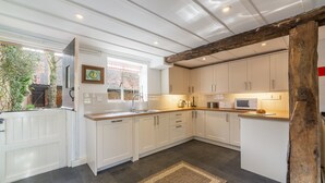 A modern kitchen with white cabinets, a wooden beam ceiling, and a view of the outside. - The Tack House, Holkham, Norfolk (Wells-Next-The-Sea)