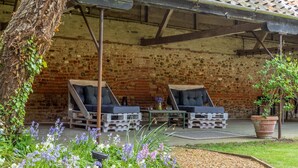 An outdoor seating area with two cushioned chairs and a table, surrounded by a brick wall and a garden with flowers. - The Tack House, Holkham, Norfolk (Wells-Next-The-Sea)
