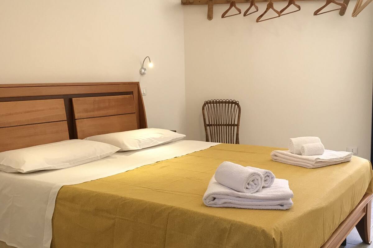 Un lit bien fait, avec une couvre-lit jaune, des oreillers blancs et des serviettes blanches pliées posées sur le bord.