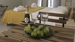 A hotel room with a bed, a bedside table with a bottle of Maschio Prosecco, two glasses, and a plate of green grapes. - Le Camere di Don Vito (Noto)