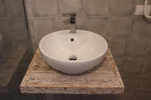 A white ceramic sink with a modern faucet on a rustic wooden shelf in a bathroom with tiled walls. - Le Camere di Don Vito (Noto)