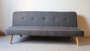 A grey sofa with wooden legs and a padded seat, featuring five buttons in different colors. - Le Camere di Don Vito (Noto)
