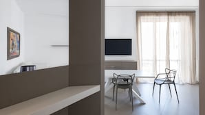 A modern living room with a flat-screen TV, a dining table with two chairs, and a large window with sheer curtains. - Design e Comfort nel centro di Catania by Wonderful Italy (Catania)