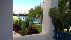 A view through a window with a pool, palm trees, and a blue railing. - Residence Jowara Smile 2897 (Mdiq)