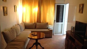 A living room with a sofa, a coffee table, and a television. There is a door leading to another room. - Residence Jowara Smile 2897 (Mdiq)