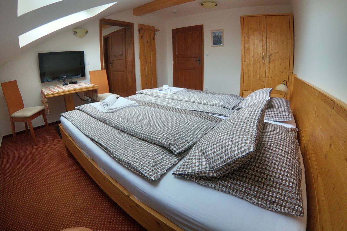 A room with a large bed, a desk, a chair, and a television.