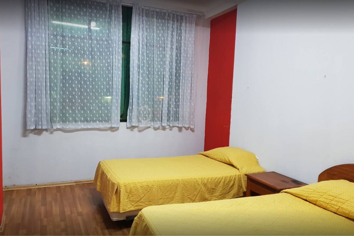 A room with two beds, each with a yellow bedspread, a window with patterned curtains, and a red wall.