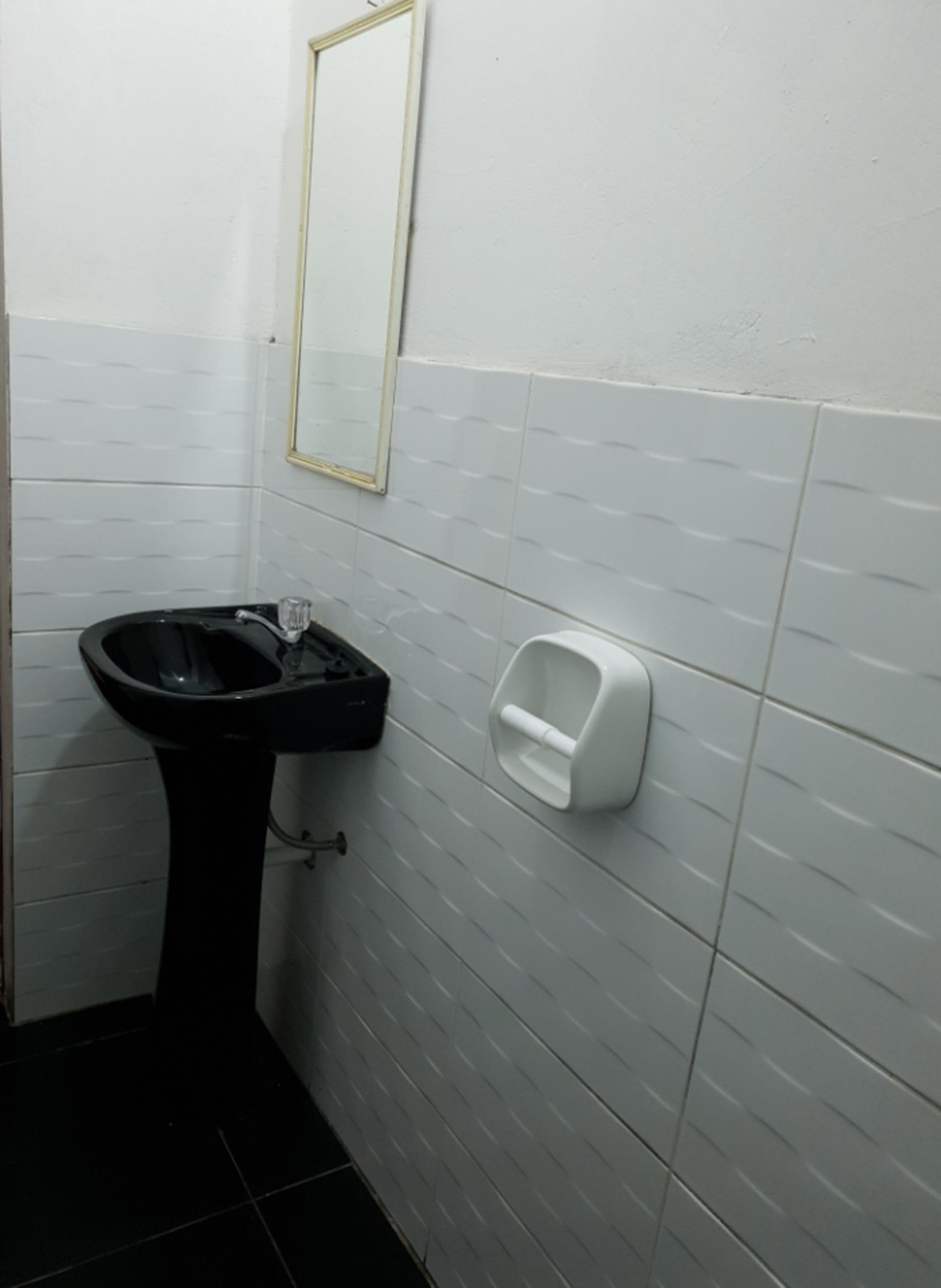 A bathroom with a black sink, a mirror, and a soap dispenser on the wall.