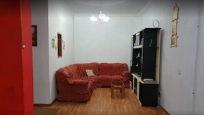 Une pièce avec un canapé d’angle rouge, une petite chaise en bois, une bibliothèque noire et un mur blanc agrémenté d’un luminaire au plafond.