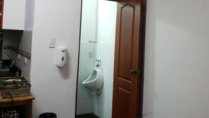 Une pièce avec une porte en bois, un urinoir, une cuisinière à gaz et une bouteille de gaz.