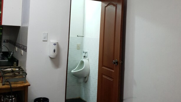 A room with a wooden door, a urinal, a gas stove, and a gas cylinder. - Casa Karmenka (Cusco)