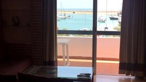 Une pièce avec une table en verre, un canapé et une vue sur les bateaux amarrés dans une marina, visible à travers une grande fenêtre.