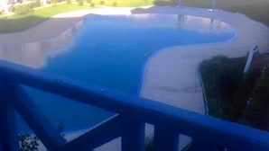 A swimming pool with a curved design, surrounded by a concrete deck and a grassy area. - Jaharasmir Residence 2905 (Mdiq)