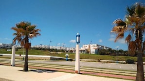 A paved walkway with palm trees, a street lamp, and buildings in the background. - Jaharasmir Residence 2905 (Mdiq)