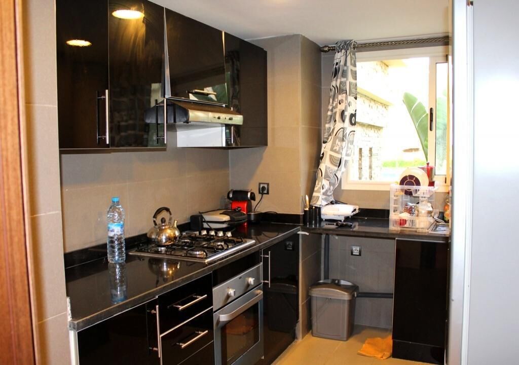 A modern kitchen with dark cabinetry, stainless steel appliances, and a window with a view of greenery.