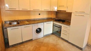 A compact kitchen with white cabinets, a built-in washing machine, a dishwasher, and a stove. - Residence Babylone Marrakech 3390 (Marrakech)