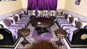 A room with a round table surrounded by sofas and ottomans, a patterned rug, and a purple curtain. - Residence Babylone Marrakech 3390 (Marrakech)