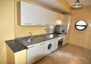 A compact kitchen with white cabinets, a granite countertop, a washing machine, and a window.