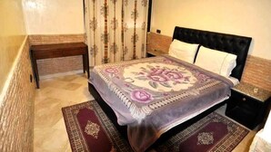 Ein Schlafzimmer mit einem Bett, einem Nachttisch, einer Bank und einem gemusterten Teppich.