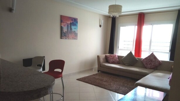 A living room with a sofa, a coffee table, a red chair, a rug, and a painting on the wall. - Atlantic Ocean Residence 3040 (Asilah)
