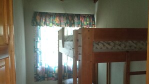 A narrow room with a wooden bunk bed, a window with patterned curtains, and a tiled floor. - Pink house (San Antonio Palopo)